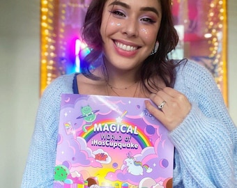 May include: A woman is holding a purple and pink book with a rainbow and the text "Magical World of iHasCupquake". The book features a cartoon cat, unicorn, and other whimsical illustrations.