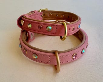 Puede incluir: Dos collares rosas con acabado mate liso y forro interior color canela. Cada collar está adornado con cristales circulares iridiscentes y rosas engastados en herrajes de metal dorado, incluyendo una hebilla, una anilla en D y una trabilla.