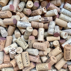 May include: A close-up image of a pile of wine corks. The corks are made of natural cork and have a variety of colors, shapes, and sizes. Some of the corks have text on them, including the names of wineries and brands. The corks are a mix of natural cork and synthetic cork.