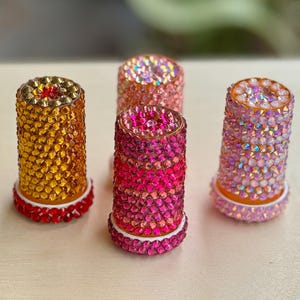 Op de afbeelding: Vier decoratieve flessenstoppers met een kristal-achtig ontwerp. De stoppers zijn in tinten roze, oranje en geel.