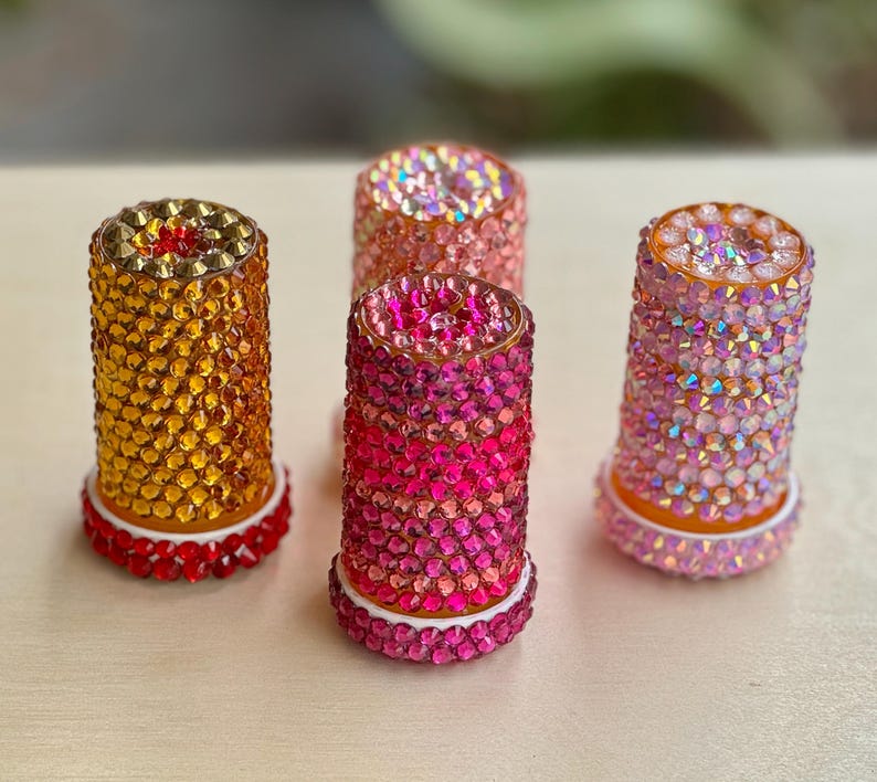 Op de afbeelding: Vier decoratieve flessenstoppers met een kristal-achtig ontwerp. De stoppers zijn in tinten roze, oranje en geel.