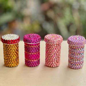 Op de afbeelding: Vier kleine, ronde containers met deksels, elk bedekt met kleurrijke strass steentjes. De containers zijn in tinten roze, geel en paars.