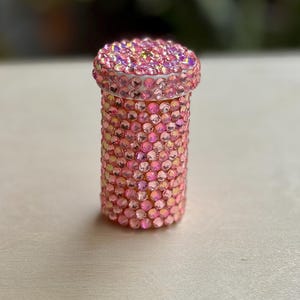 Op de afbeelding: Een roze pillenflesje bedekt met iriserende strass steentjes.