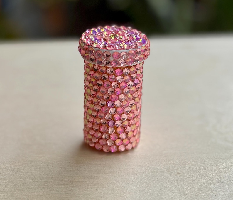 Op de afbeelding: Een roze pillenflesje bedekt met iriserende strass steentjes.
