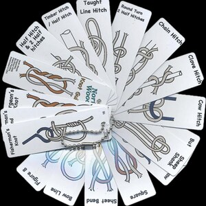 May include: A white knot guide with various knot diagrams, including the "Timber Hitch," "Chain Hitch," and "Bow Line." Each card features a knot illustration and its name. The cards are connected by a metal ring, creating a fan-like display.