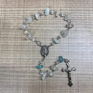 May include: A white and blue glass bead rosary with a silver crucifix and a silver charm of the Virgin Mary.