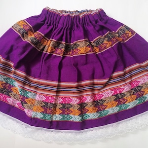 Puede incluir: Una falda morada con un patrón geométrico colorido y un borde de encaje blanco.