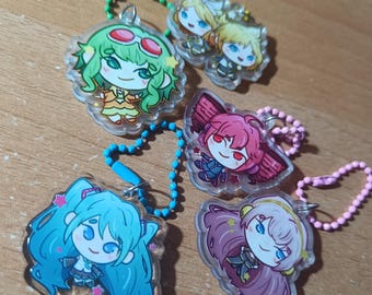 May include: A collection of five acrylic charm keychains featuring anime-style characters. Each charm has a unique character design with vibrant colors, attached to a beaded chain. The keychains are on a wooden surface.