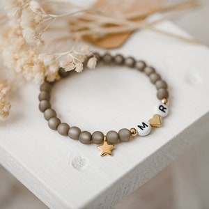 May include: A gray beaded bracelet with gold accents and white letter beads spelling "MR" with a gold heart charm and a gold star charm.