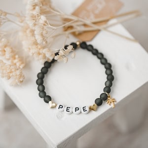 May include: A black beaded bracelet with a gold palm tree charm and white letter beads spelling "PEPE".