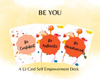 Op de afbeelding: Een set van 52 zelfversterkende kaarten met kleurrijke aquarel-spetterontwerpen. De kaarten bevatten de woorden "Be You" bovenaan en drie kaarten worden getoond met de woorden "Be Confident", "Be Authentic" en "Be Unashamed".