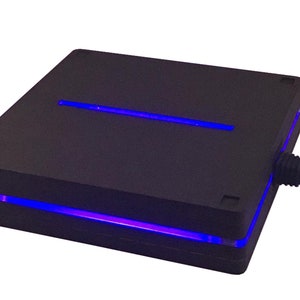 Könnte beinhalten: Ein schwarzes rechteckiges Gerät mit einem blauen Lichtstreifen am unteren Rand und einem blauen Lichtstreifen oben. Das Gerät hat ein schwarzes Kabel an der Seite.