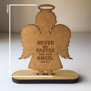 May include: Wooden angel figurine with wings and a halo. The angel is standing on a base and has the text "NEVER RIDE FASTER THAN YOUR ANGEL CAN FLY" engraved on its chest.