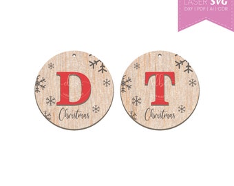 May include: Two round wooden ornaments with a rustic woodgrain finish. Each ornament features a large red letter, "D" and "T", and the word "Christmas" in black script. The ornaments are decorated with small snowflake designs.