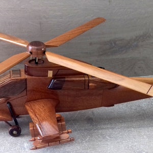 Peut inclure: Modèle en bois d'un hélicoptère avec une peinture brune et beige. Le modèle a un rotor principal et un rotor de queue rotatifs. Le modèle est en bois et a une apparence réaliste.