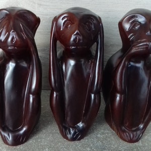 May include: Three dark brown wooden monkey figurines, each with a different gesture: one covering its eyes, one covering its ears, and one covering its mouth. The monkeys are carved in a realistic style and have a glossy finish.