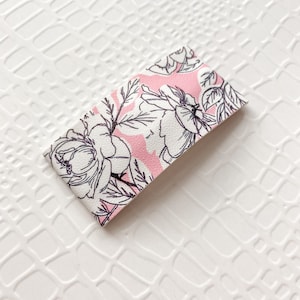 May include: A white and pink floral patterned hair clip. The clip is rectangular and has a smooth, glossy finish.