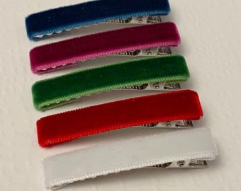 May include: A set of five rectangular hair clips, each covered in soft velvet fabric. The clips are arranged in a vertical stack and feature distinct colors: navy blue, magenta, forest green, bright red, and white. Each clip has a silver metal base.