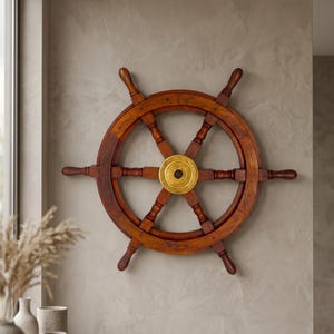 May include: A wooden ship's wheel with a brass center, mounted on a textured gray wall. The wheel is a rich brown color and has six spokes. A nautical-themed decorative item.