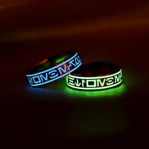 May include: Two glow-in-the-dark rings with the word "LOVE" inscribed in white on a black background. The rings are glowing blue and green.