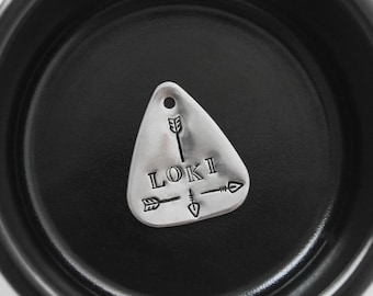 May include: Silver triangular tag with the name "LOKI" engraved in a simple font. Three arrows are engraved above and below the name.