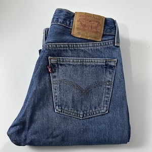 Puede incluir: Vaqueros de mezclilla azul doblados con un bolsillo trasero y un parche de cuero marrón. El parche dice "LEVI STRAUSS & CO. ORIGINAL RIVETED QUALITY CLOTHING". Los vaqueros tienen una etiqueta roja en el bolsillo trasero.