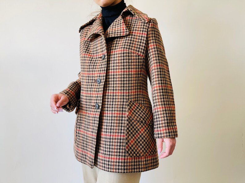 May include: A vintage coat with a classic houndstooth pattern in tan, black, and red. The coat features a notched collar, button closure, and two front pockets. The coat is a mid-length style.