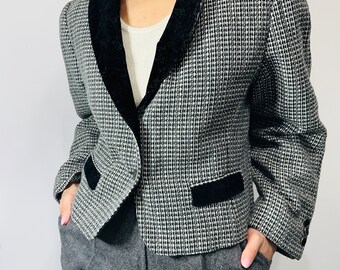 May include: A black and white houndstooth blazer with a black velvet collar and pocket trim. The blazer has a single-button closure and padded shoulders. The model is wearing grey trousers.