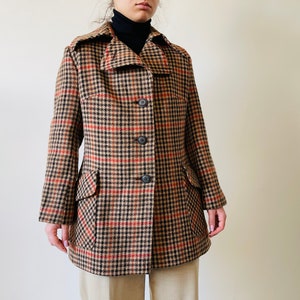 May include: A vintage houndstooth coat in brown, black, and red. The coat has a notched collar, three buttons, and two front pockets. The coat is knee-length and has a classic, tailored fit.
