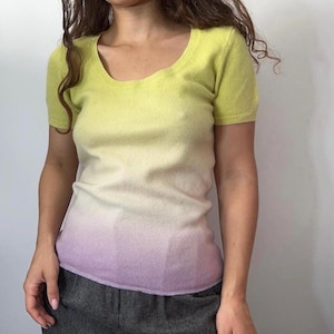 Può includere: Un top a maniche corte con scollo tondo e sfumatura di colore. La parte superiore passa da un giallo chiaro sulle spalle a un delicato lavanda sull'orlo. Il tessuto sembra essere una maglia fine, che offre una vestibilità liscia e aderente.