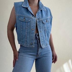 Può includere: Gilet in denim blu chiaro con collo e chiusura con bottoni. Il gilet presenta due tasche frontali e una vestibilità corta. Il gilet è abbinato a jeans blu chiaro. Un outfit classico e casual.