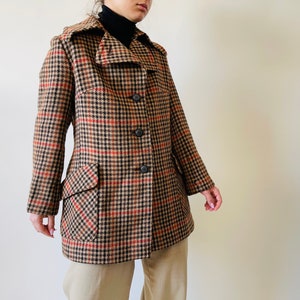 May include: A brown, black, and red plaid coat with a notched collar, two front pockets, and three black buttons. The coat is knee-length and has a classic, tailored design.