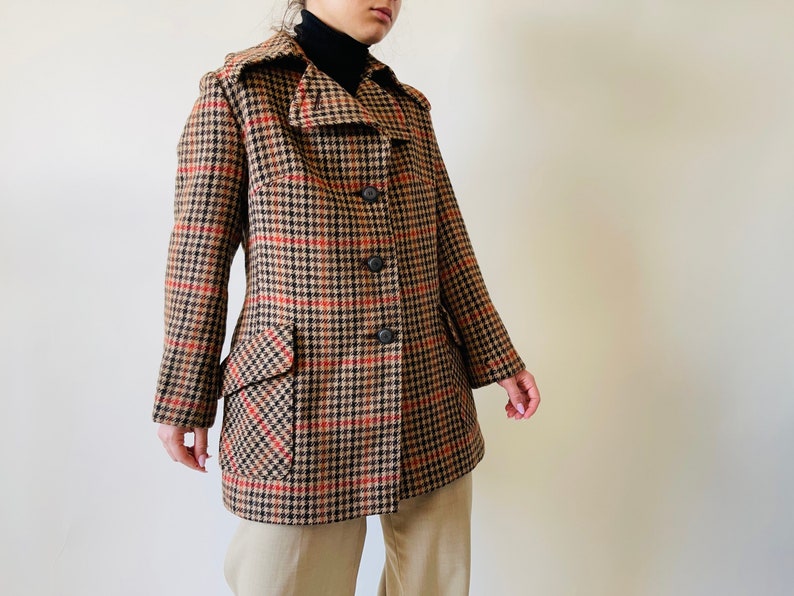 May include: A brown, black, and red plaid coat with a notched collar, two front pockets, and three black buttons. The coat is knee-length and has a classic, tailored design.
