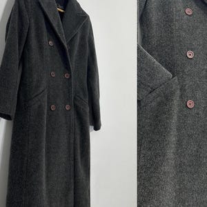 May include: A charcoal gray double-breasted wool coat with a notched collar and two rows of buttons. The long coat has two front pockets and is hanging on a wooden hanger.