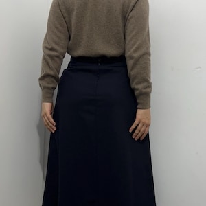May include: A beige long-sleeved turtleneck sweater paired with a solid navy blue midi-length skirt. The sweater features a ribbed collar and cuffs, while the skirt has a smooth, plain finish with a visible center seam and a button closure at the waist.