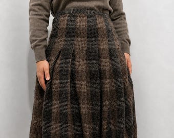 May include: A brown long-sleeved sweater paired with a knee-length pleated skirt featuring a dark brown and black checkered pattern. The skirt has a high-waisted design with vertical pleats that create a full, structured silhouette.