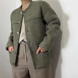May include: Olive green wool jacket with a round collar and silver buttons. The jacket has two front pockets and decorative stitching across the chest. The sleeves are long and the jacket is buttoned up.