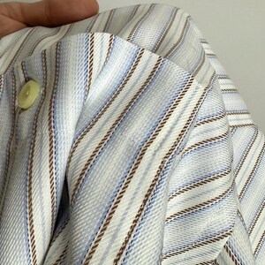 May include: A light blue and white striped shirt with brown accent stripes. The shirt has a buttoned cuff and a light green button. The fabric is folded, showing the texture and pattern of the material.