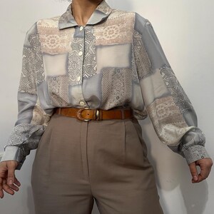 Könnte beinhalten: Eine Vintage-Patchwork-Bluse in Blau-, Beige- und Grautönen mit Paisley- und Blumenmuster. Das langärmlige Hemd ist geknöpft und wird mit einer braunen Hose und einem braunen Ledergürtel kombiniert.