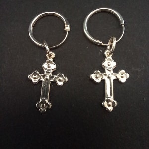 May include: A pair of silver hoop earrings with dangling cross pendants. Each cross features a detailed floral design at the ends of the arms and the top of the cross. The earrings are displayed against a dark background.