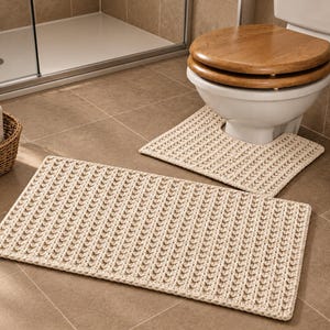 Peut inclure: Un ensemble de deux tapis de salle de bain de couleur beige clair, comprenant un tapis rectangulaire et un tapis de contour en forme de U conçu pour s'adapter à la base des toilettes. Les deux pièces présentent un motif texturé en crochet.