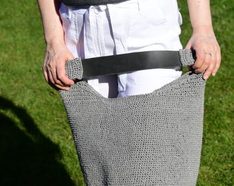 May include: A grey crocheted hobo bag featuring a wide, smooth black leather strap attached to the body with matching grey crocheted connectors. The bag has a textured, woven appearance and a deep, open-top design for carrying personal items.
