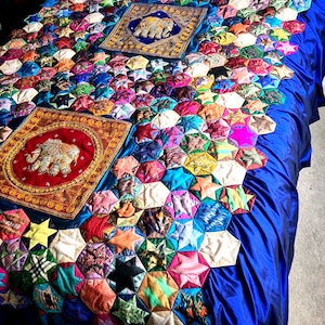 May include: A blue and white quilt with a star pattern. The quilt is made of many different fabrics and colours. There are two embroidered cushions with elephants on them.