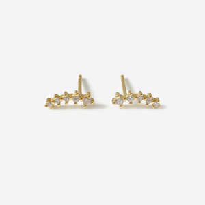 May include: A pair of gold-coloured stud earrings. Each earring has a curved design with multiple small, clear gemstones. The earrings are displayed on a white background. The text "HYANGMI GU Jewelry" is at the bottom.