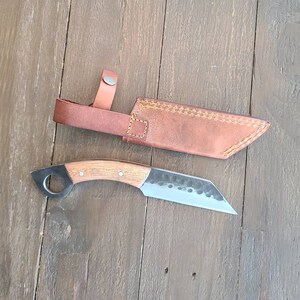 以下が含まれることがあります： 木製のハンドルとステンレス鋼の刃を備えた手作りのナイフ。茶色の革製の鞘が付属しています。ナイフはハンドルの端にリングが付いたユニークなデザインです。鞘にはスナップ付きのストラップが付いています。