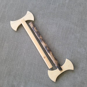 May include: Two wooden toy axes. One axe is fully assembled with a light wood handle and a double-bladed head. The other axe is disassembled, with a separate handle and head. The handle is dark brown and the head is light wood.