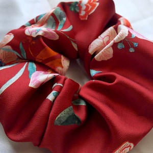 Op de afbeelding: Een rode scrunchie met een bloemenprint met witte, roze en groene bloemen.