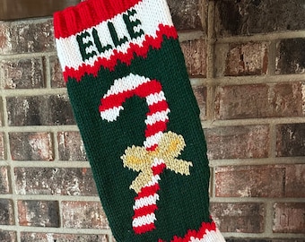 May include: A green, white and red knitted Christmas stocking with the name "ELLE" at the top and a candy cane with a gold bow on the front.