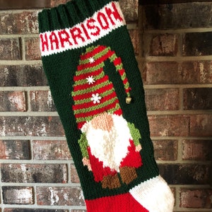 May include: A green, red and white knitted Christmas stocking with a gnome design and the name "HARRISON" embroidered on the top.