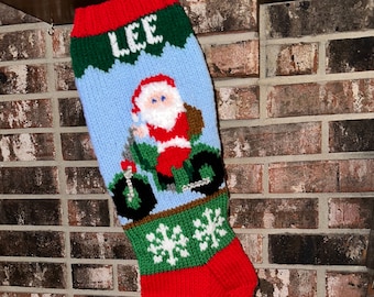 May include: A red, green and blue knitted Christmas stocking with the name "LEE" at the top and a design of Santa Claus riding a motorbike.